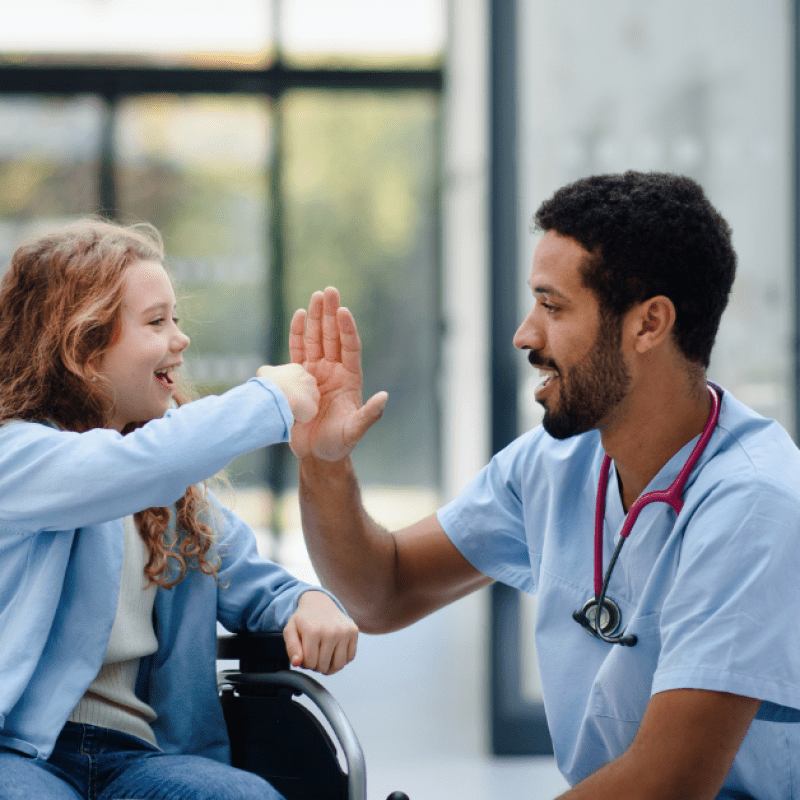 nurse high-fiving a patient in wheelchair - How Pediatric Home Care Nurses Can Help Patients Gain Independence